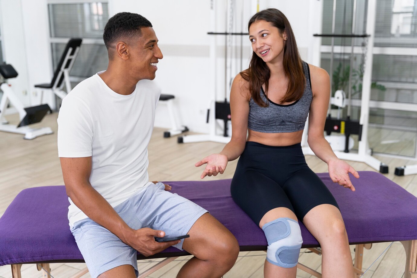 Sports physical therapy clinic with exercise equipment, physiotherapists working with patients, and rehabilitation tools