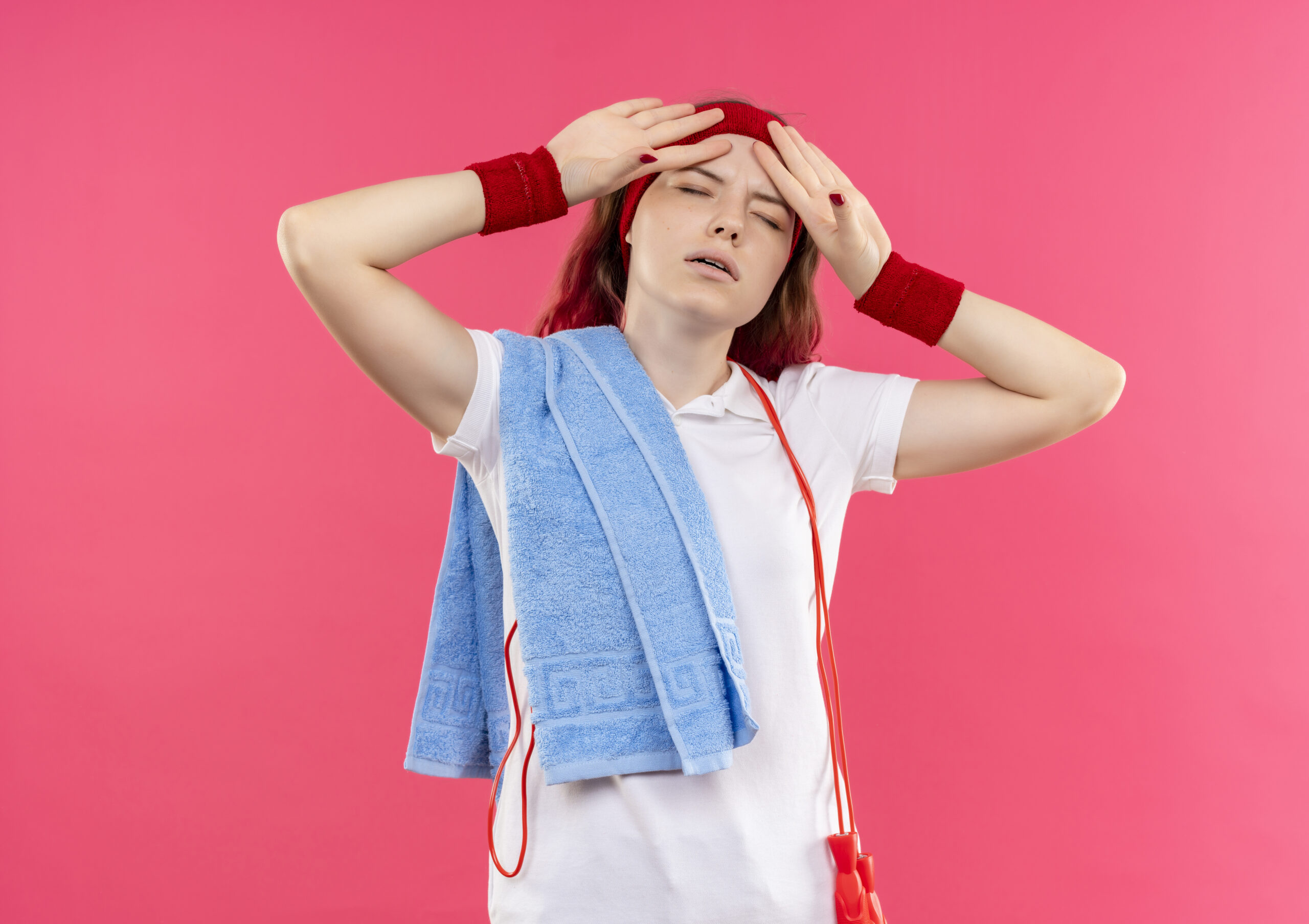 Woman experiencing heat exhaustion and fatigue after exercise while holding her forehead with a towel over her shoulder.