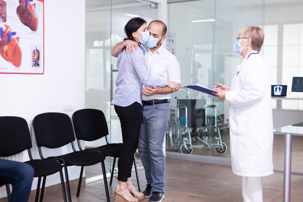 Doctor speaking with a couple embracing each other in a hospital consultation room after receiving important medical news.